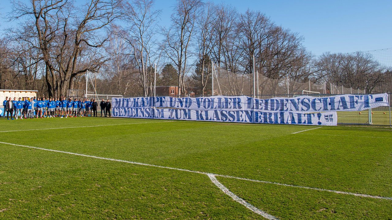 The Hertha players stand in front of the fan banner at Schenckendorffplatz