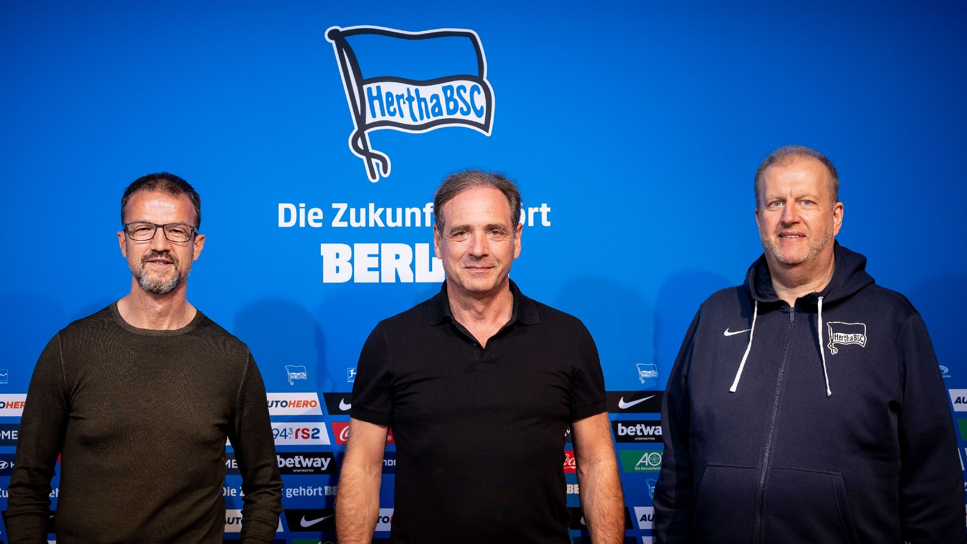 Fredi Bobic, Carsten Schmidt und Ingo Schiller stehen nebeneinander vor der Hertha-Fahne.