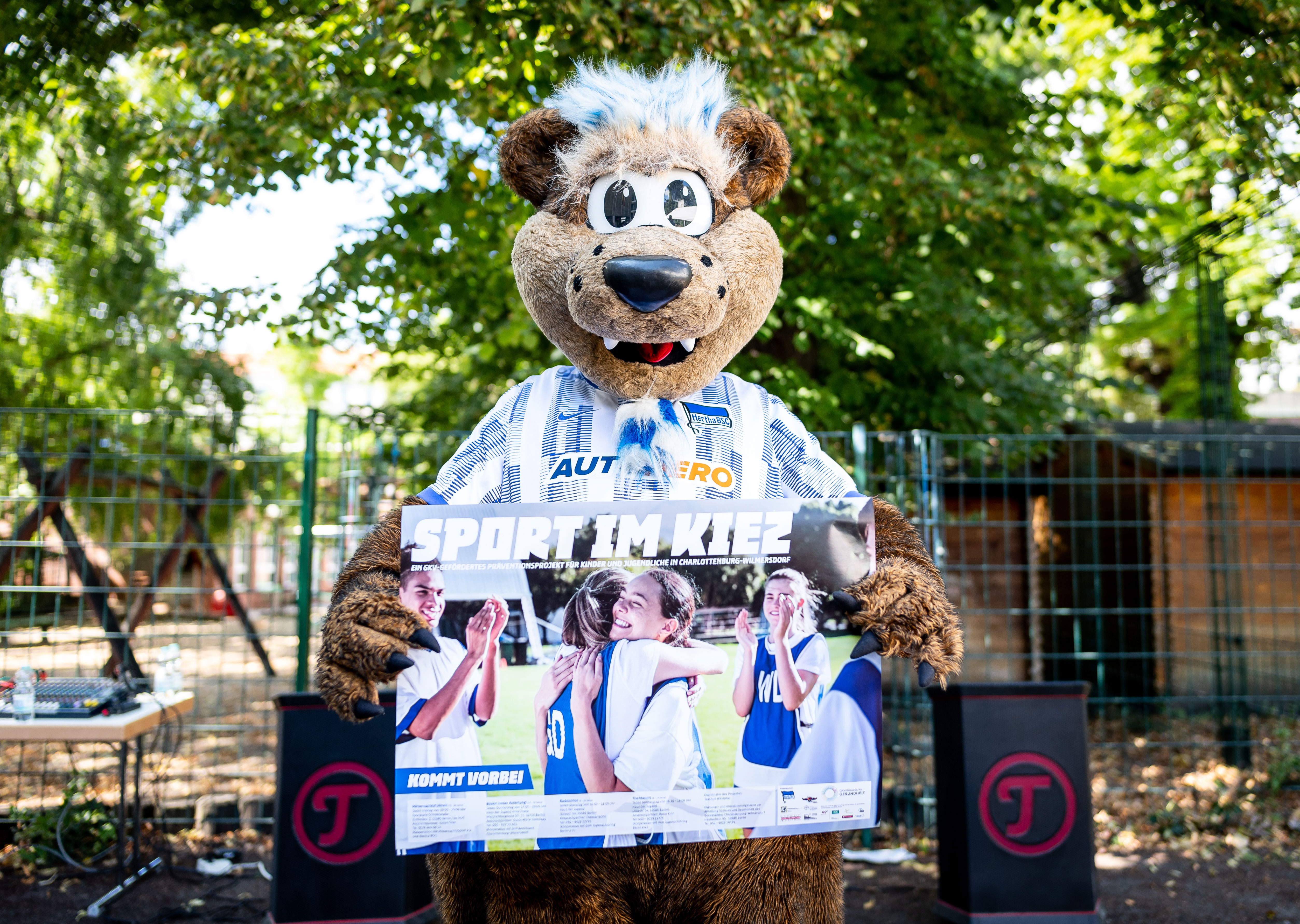 Herthinho posiert mit dem Flyer von 'Sport im Kiez'.