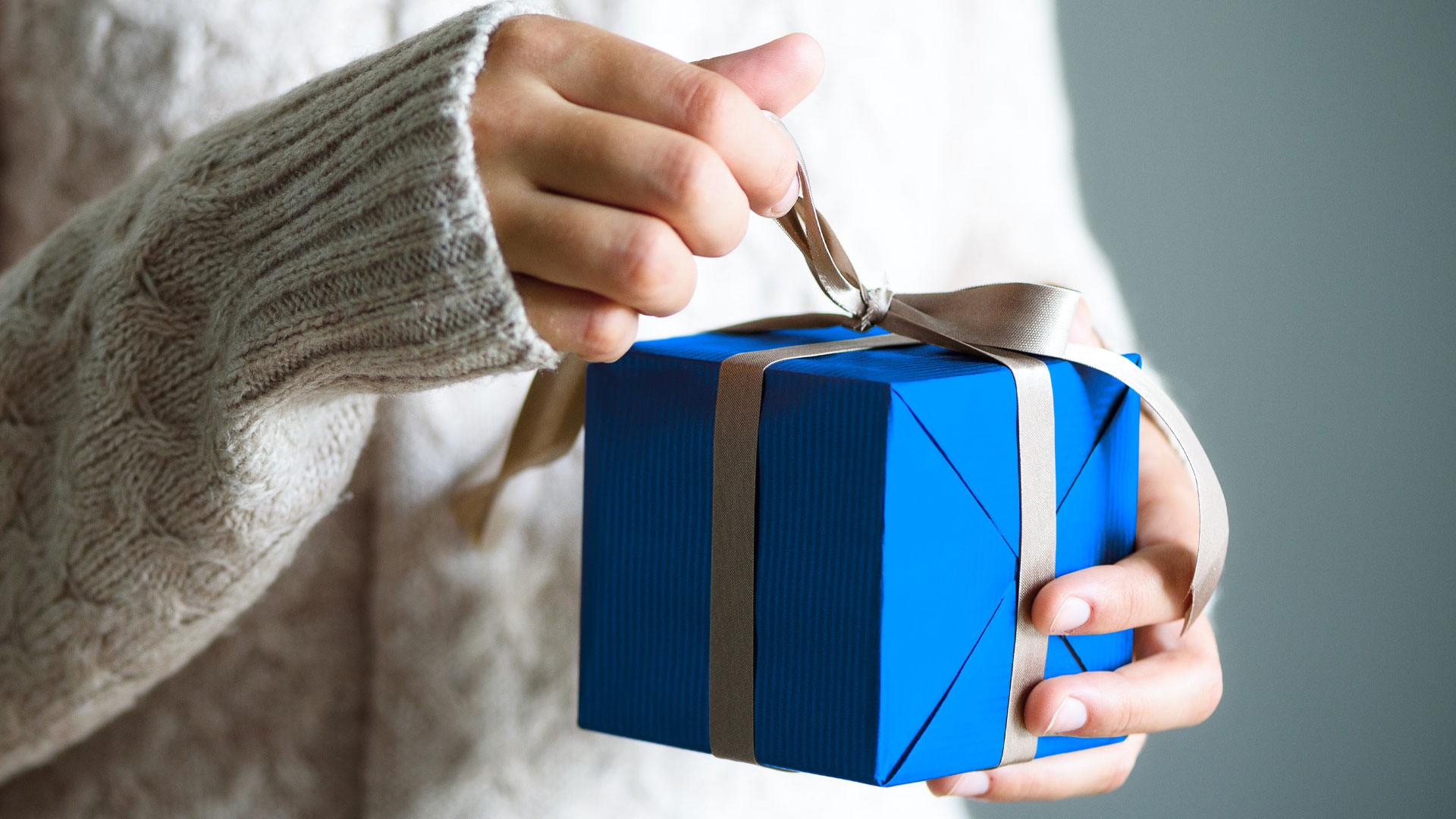 Eine Person öffnet das blau-weiße Geschenk.