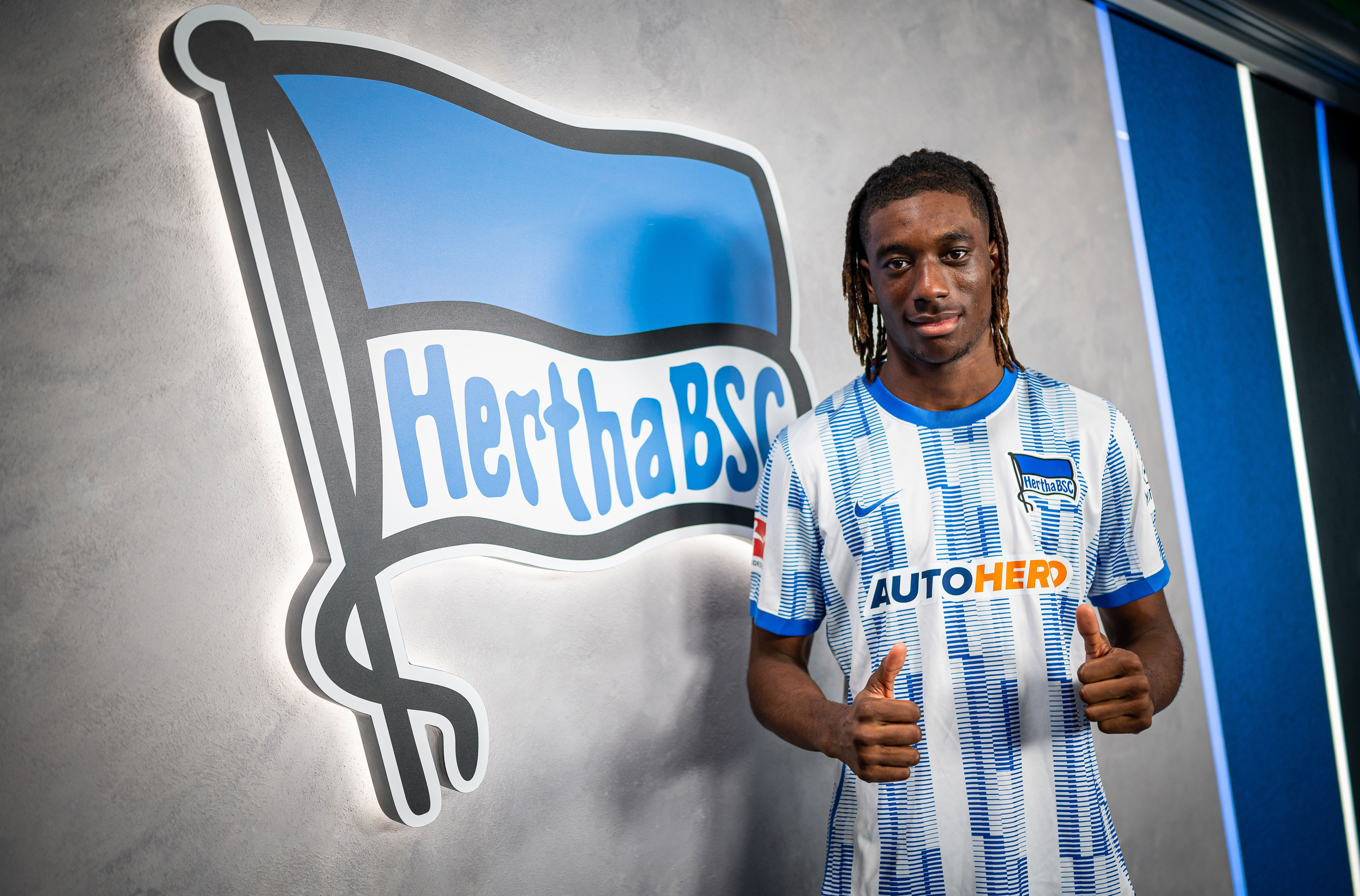 Kélian Nsona posiert im Hertha-Trikot vor unserem Vereinslogo.