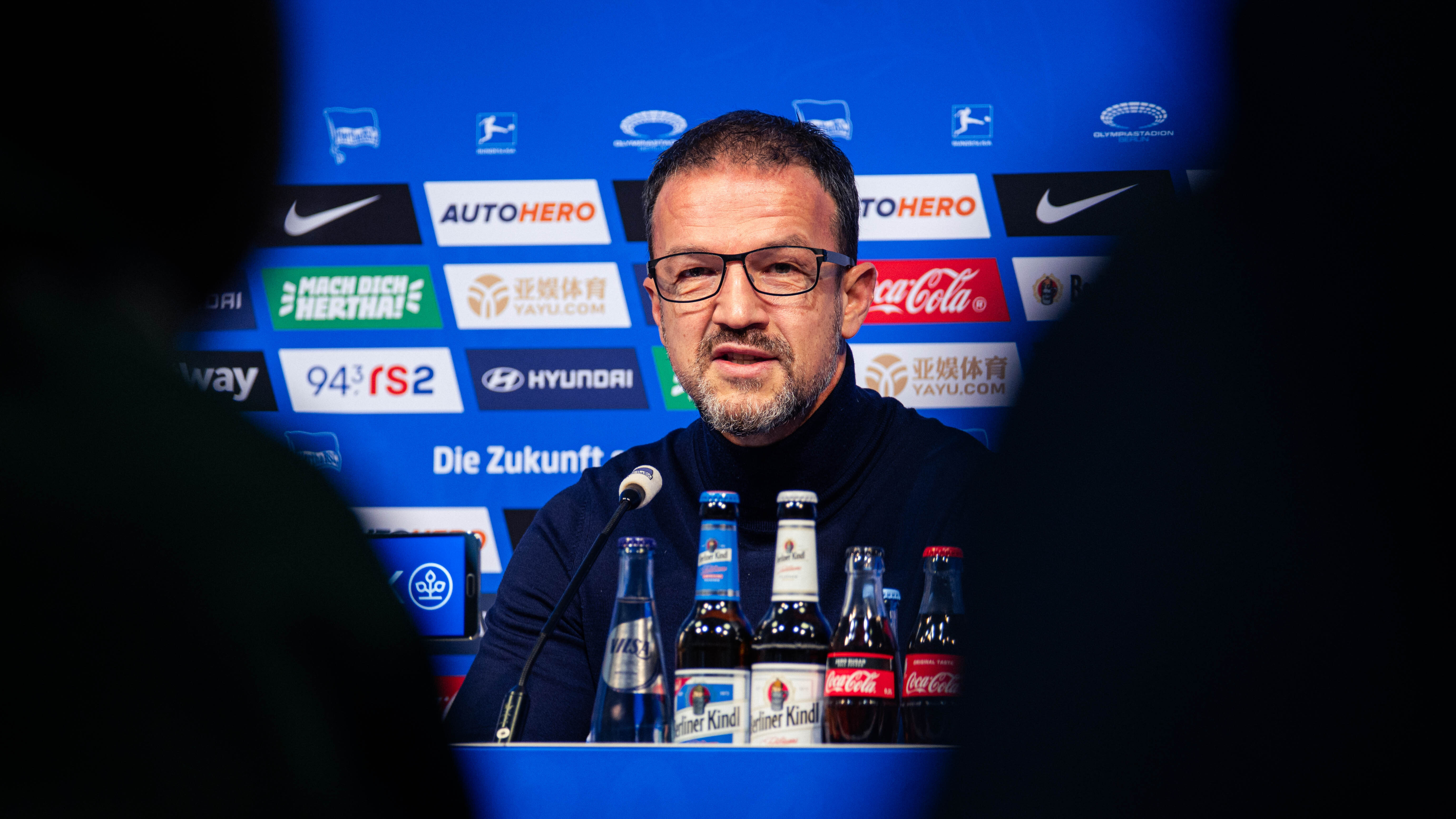 Fredi Bobic sitzt auf dem Podium und schaut in die Kamera.