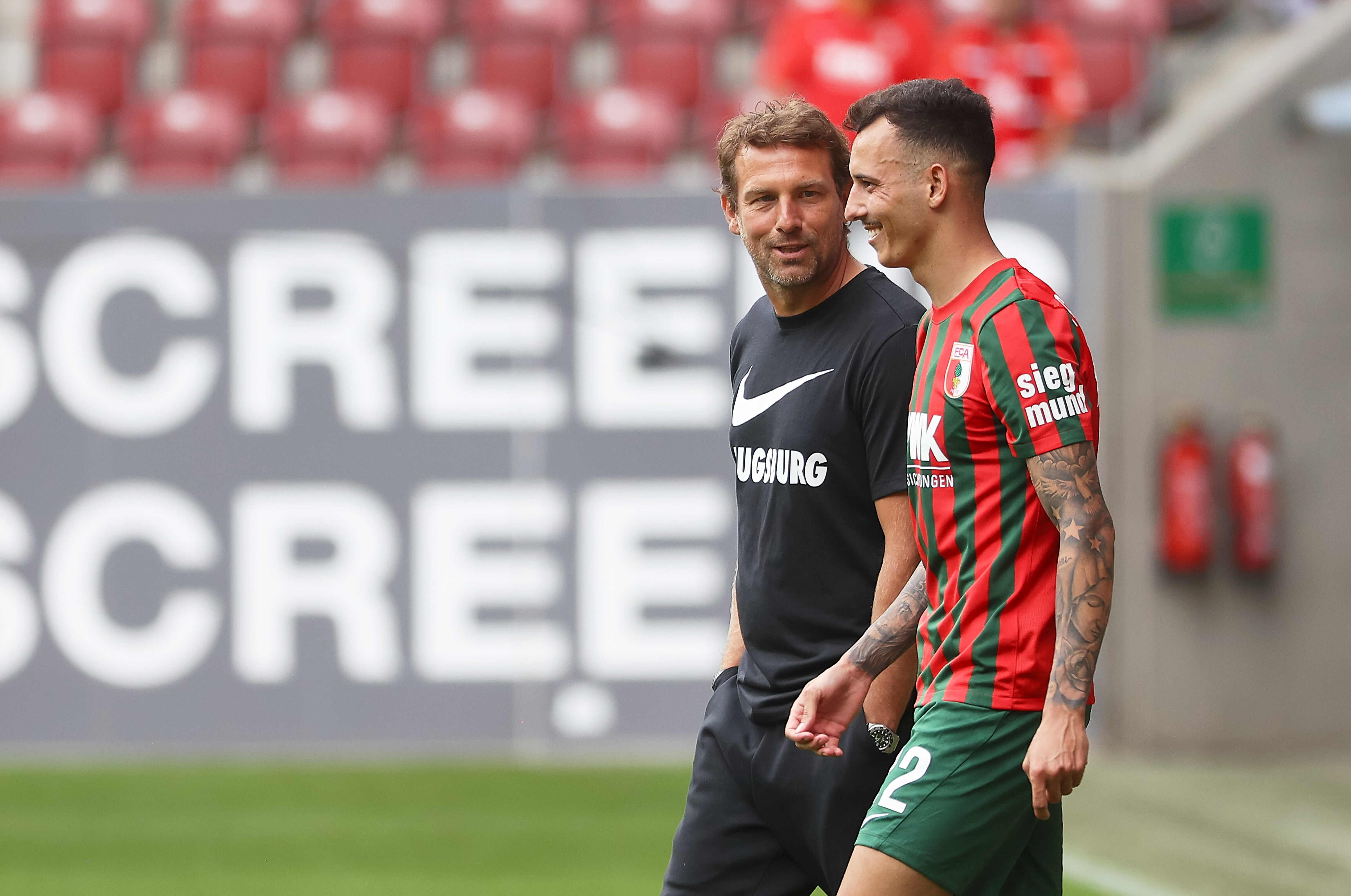 Markus Weinzierl tauscht sich lächelnd mit FCA-Profi Iago aus.