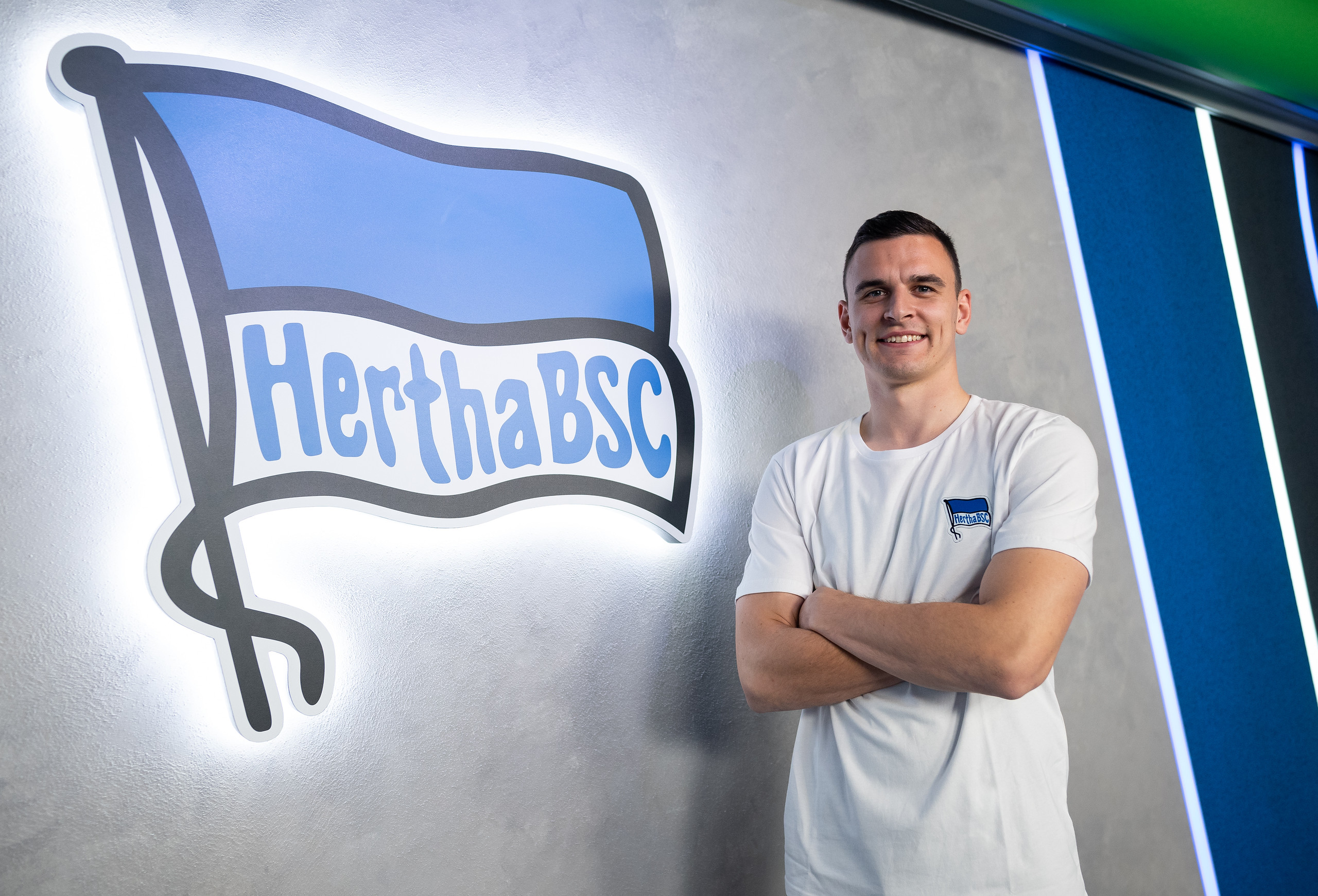 Filip Uremović posiert lächelnd vor der Hertha-Fahne.