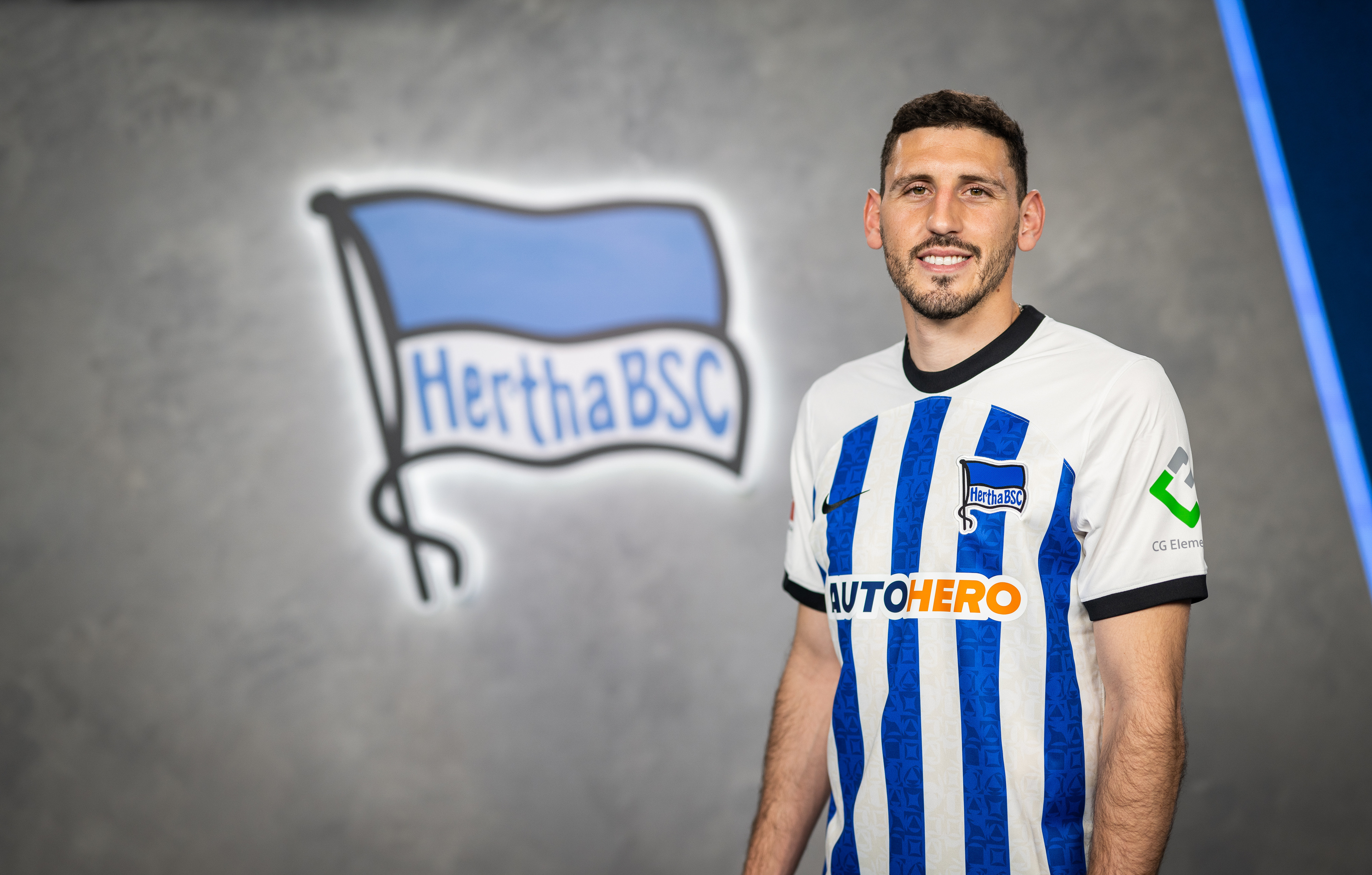 Agustín Rogel wearing the Hertha shirt in front of the club logo.