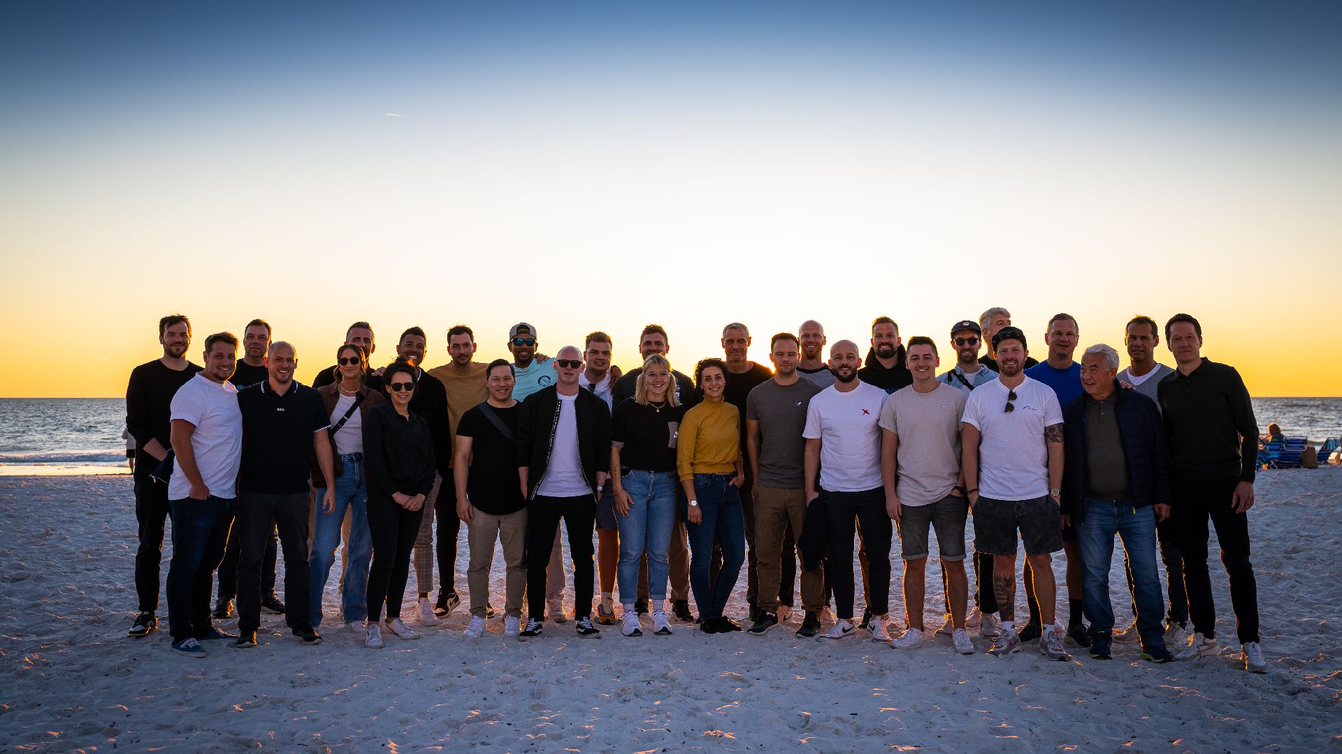 Trainerteam, Staff und Clubmedien posieren zusammen am Strand.