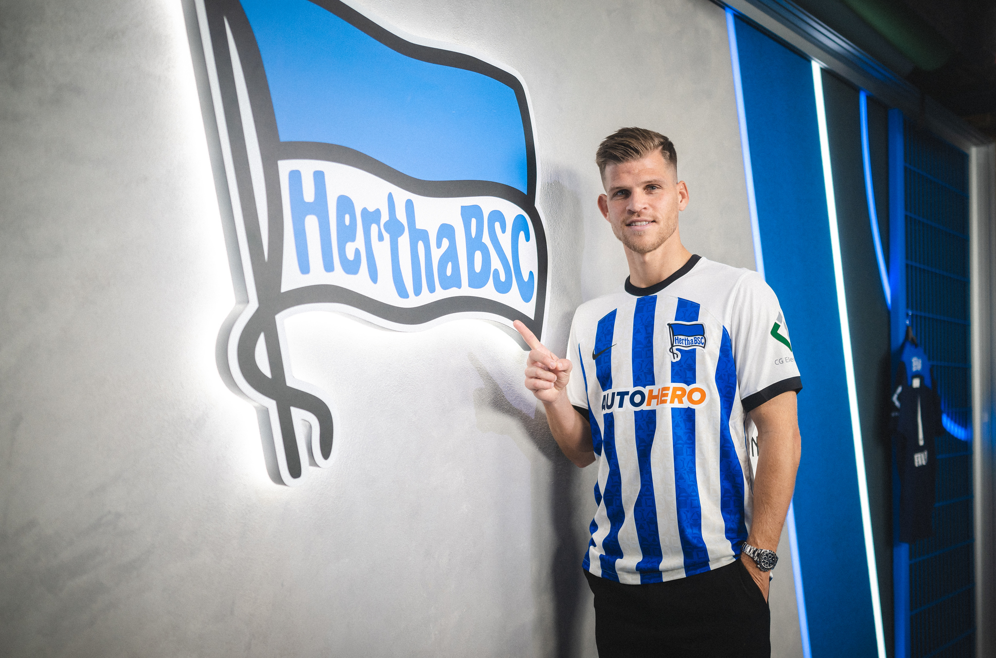 Florian Niederlechner posiert im Hertha-Trikot vor unserer Fahne.