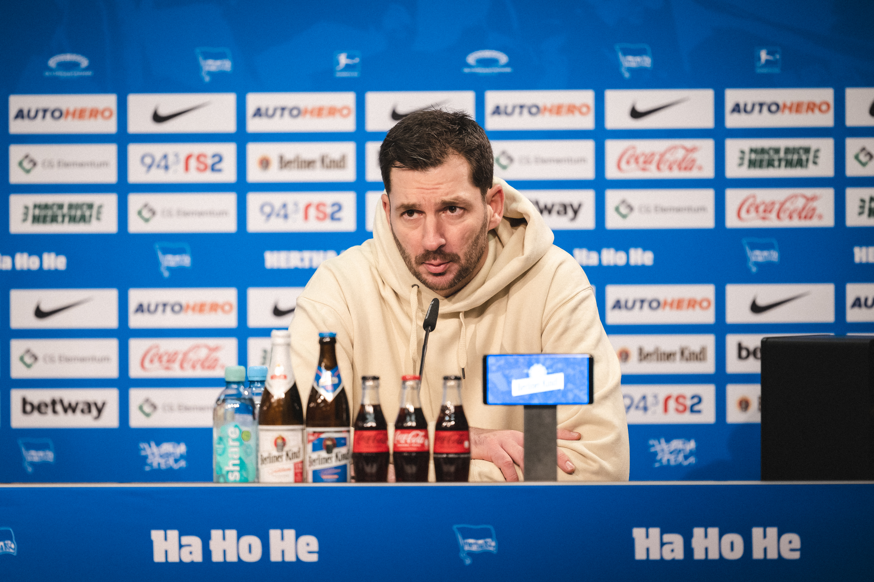Sandro Schwarz sitzt bei einer Pressekonferenz auf dem Podium.