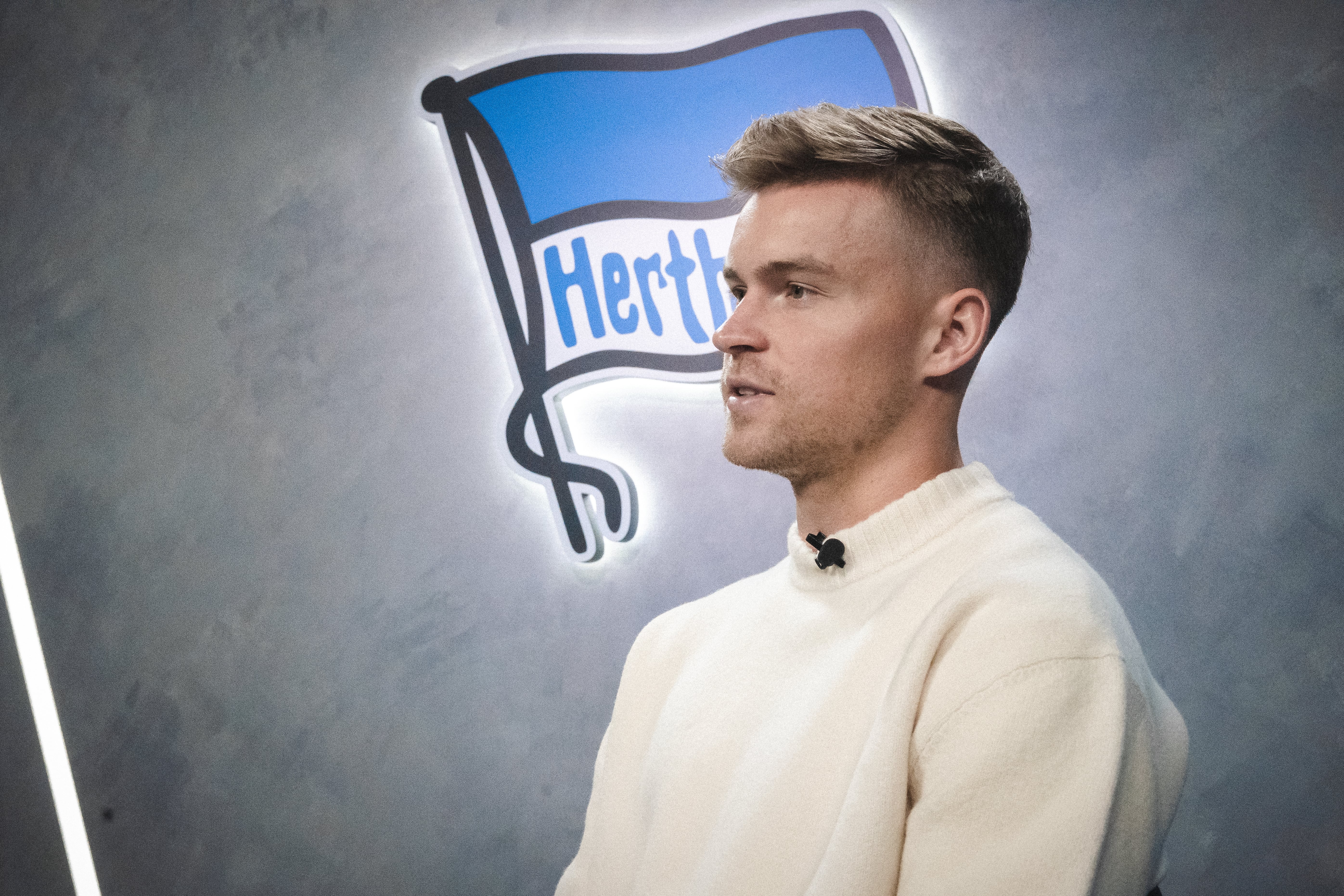 Maximilian Mittelstädt sitzt vor der Hertha-Fahne in unserer Traumfabrik.