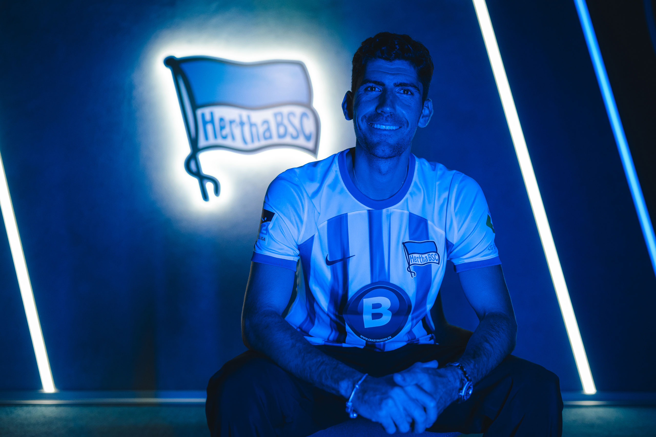 Andreas Bouchalakis sitzt lächelnd im Hertha-Trikot in der Traumfabrik.