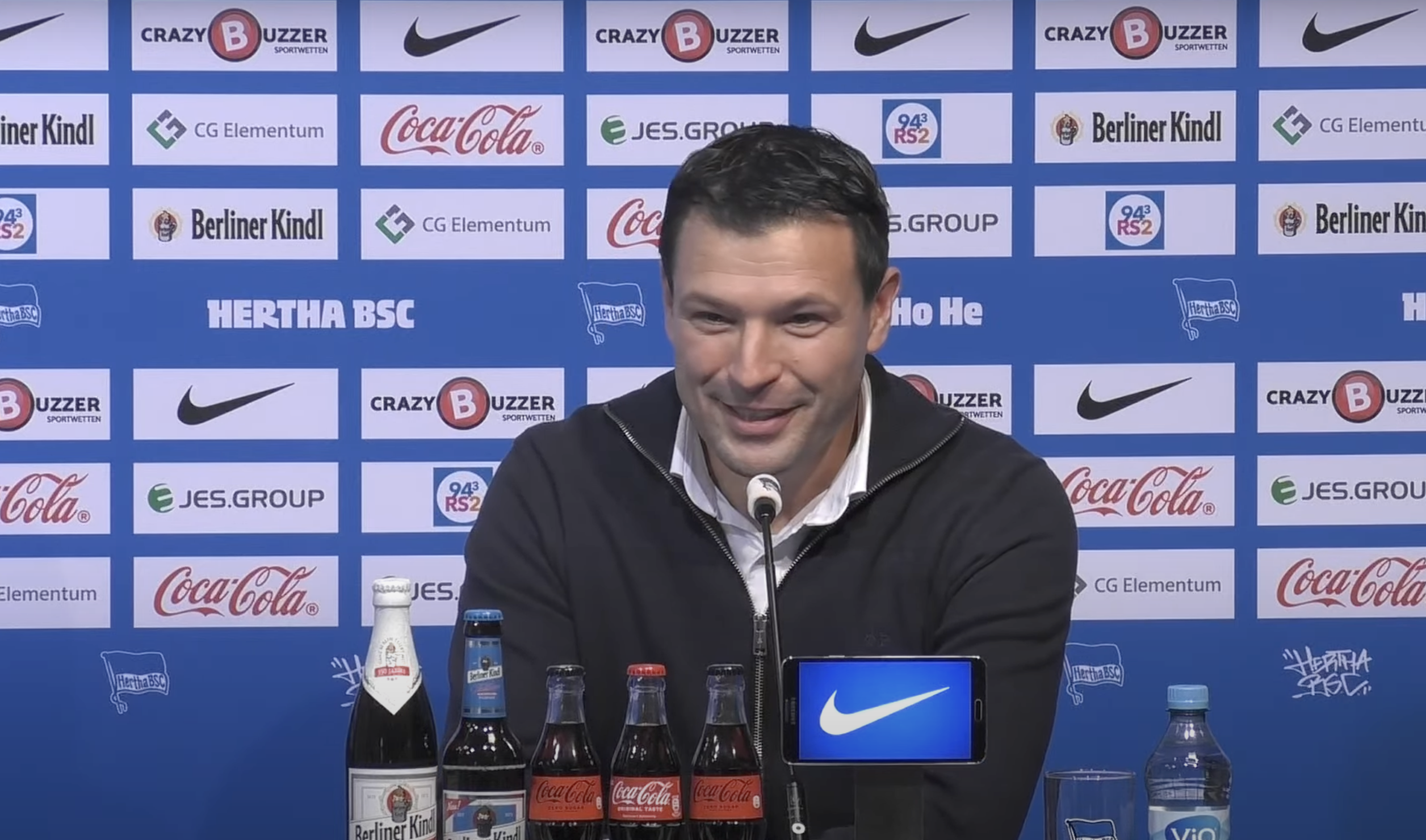 Benjamin Weber sitzt bei der Pressekonferenz auf dem Podium und lächelt.
