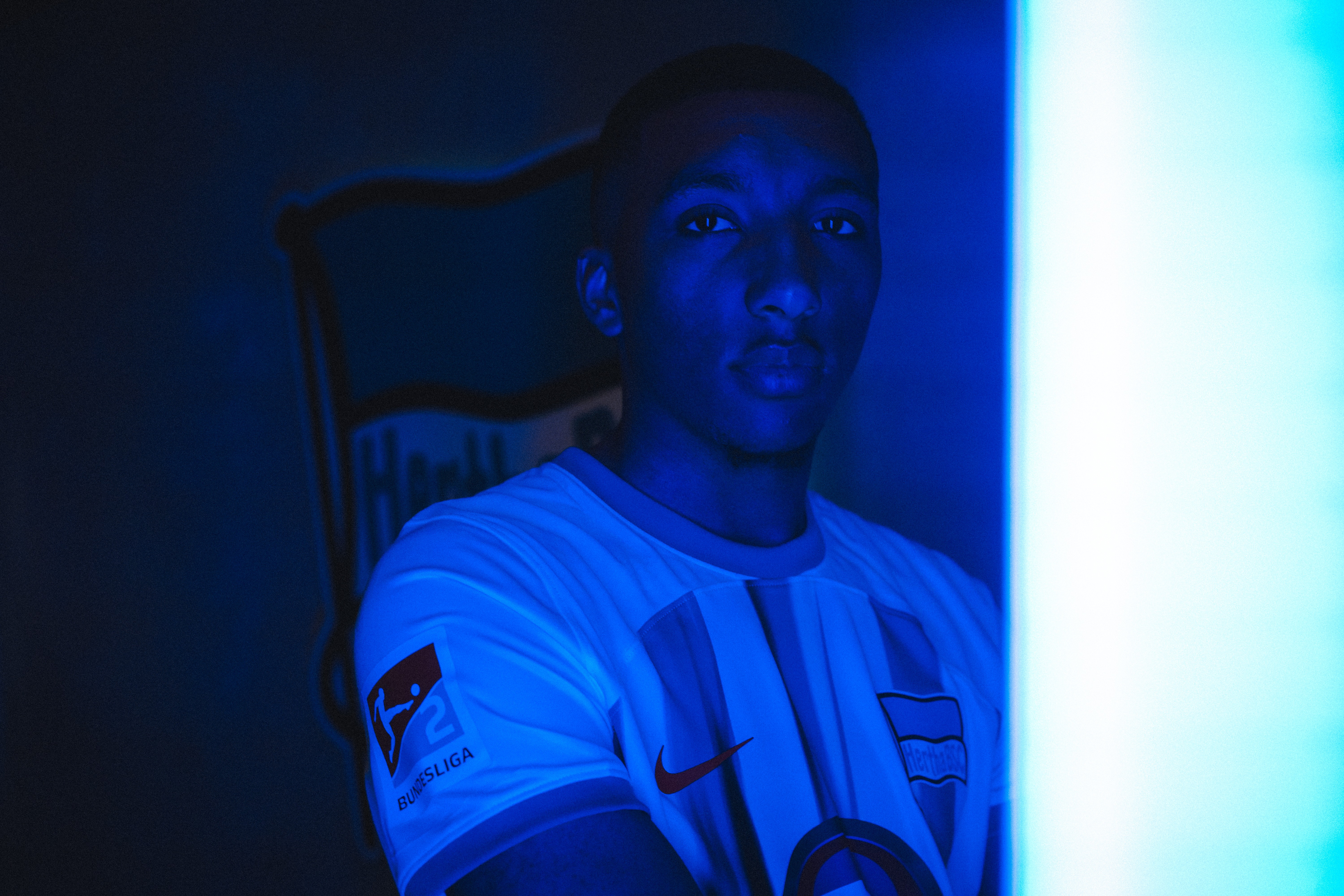Bradley Ibrahim wearing a Hertha shirt, illuminated by blue light.