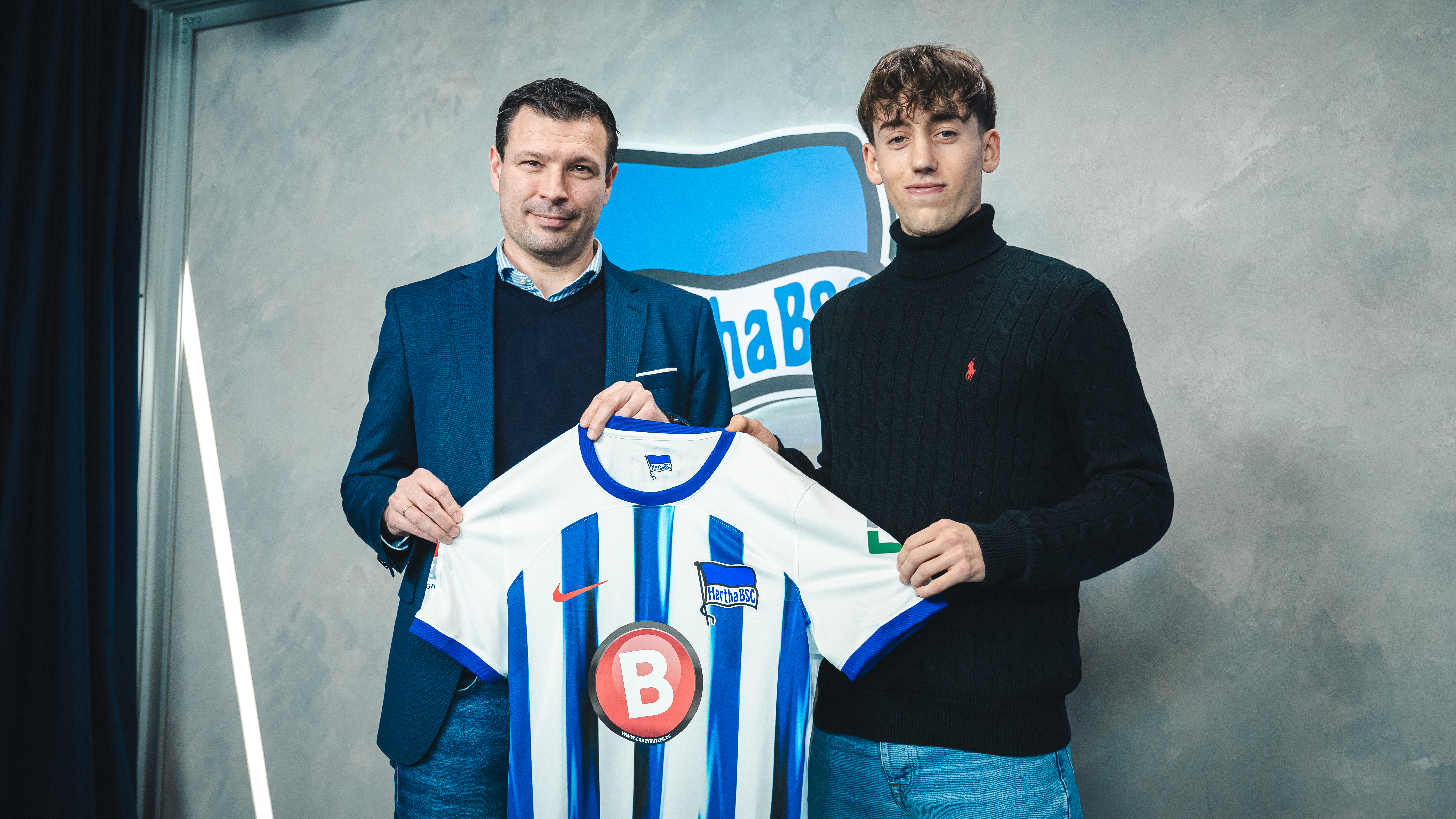 Tim Hoffmann and sporting director Benjamin Weber hold a Hertha shirt aloft in front of the camera.