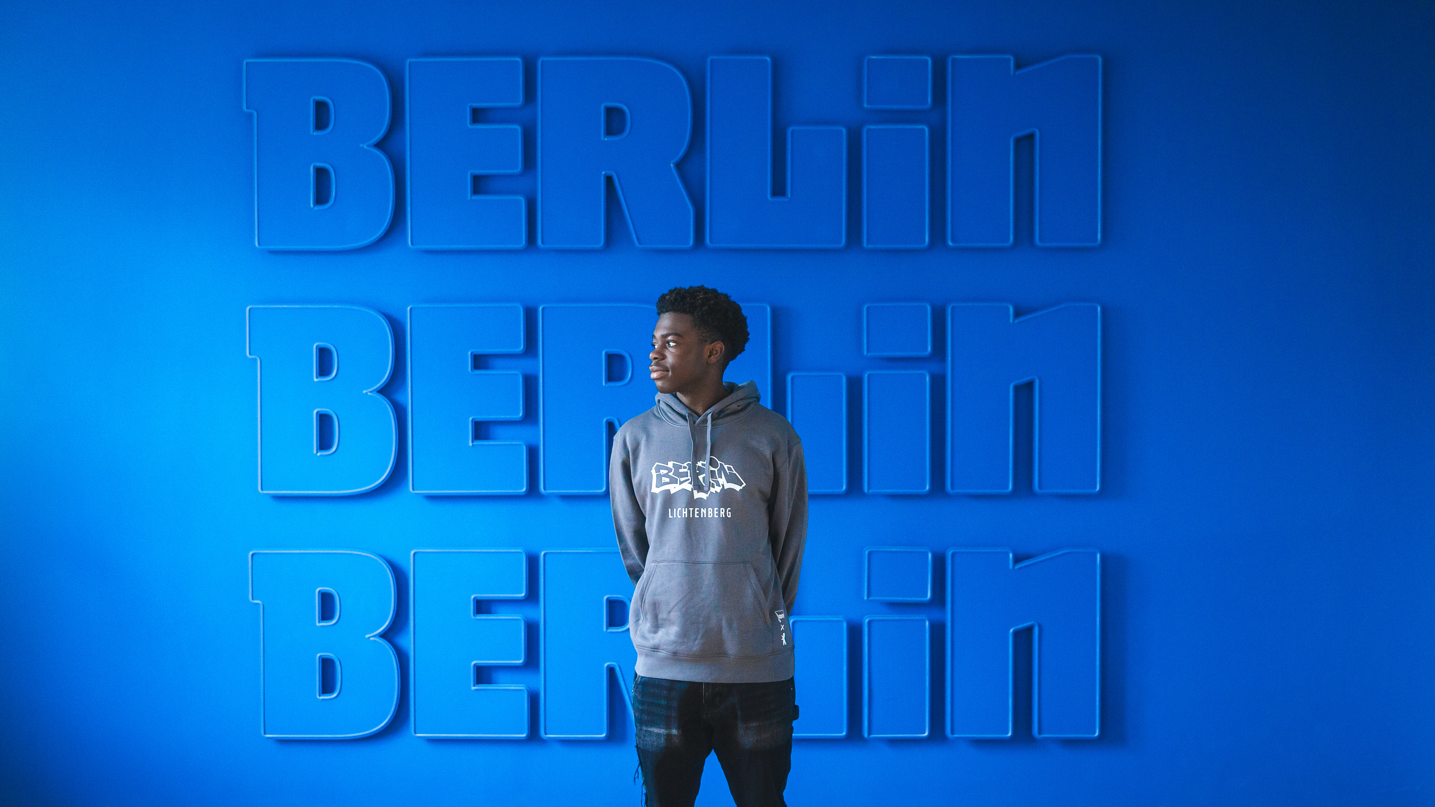 Boris Mamuzah Lum vor der blau-weißen Wand an der Geschäftsstelle.