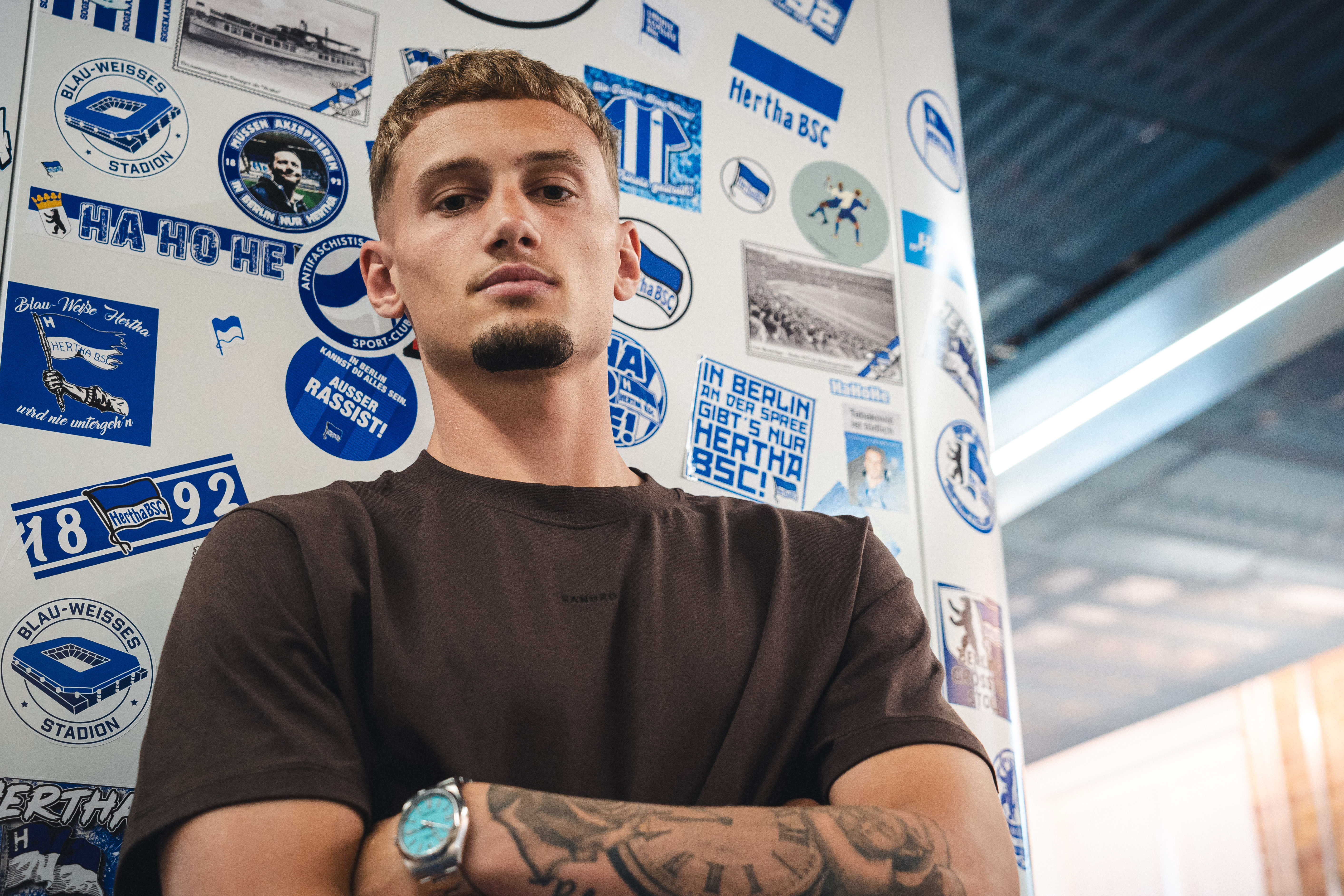 Michaë Cuisance lehnt an eine Wand voller Hertha-Aufkleber.