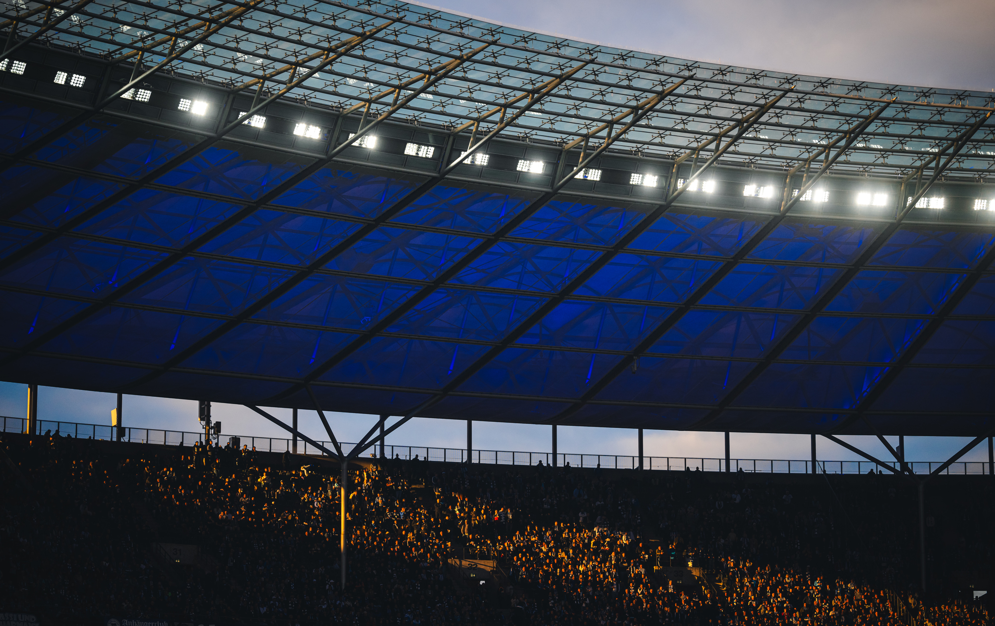 Fans im Sonnenuntergang auf der Tribüne im Olympiastadion.