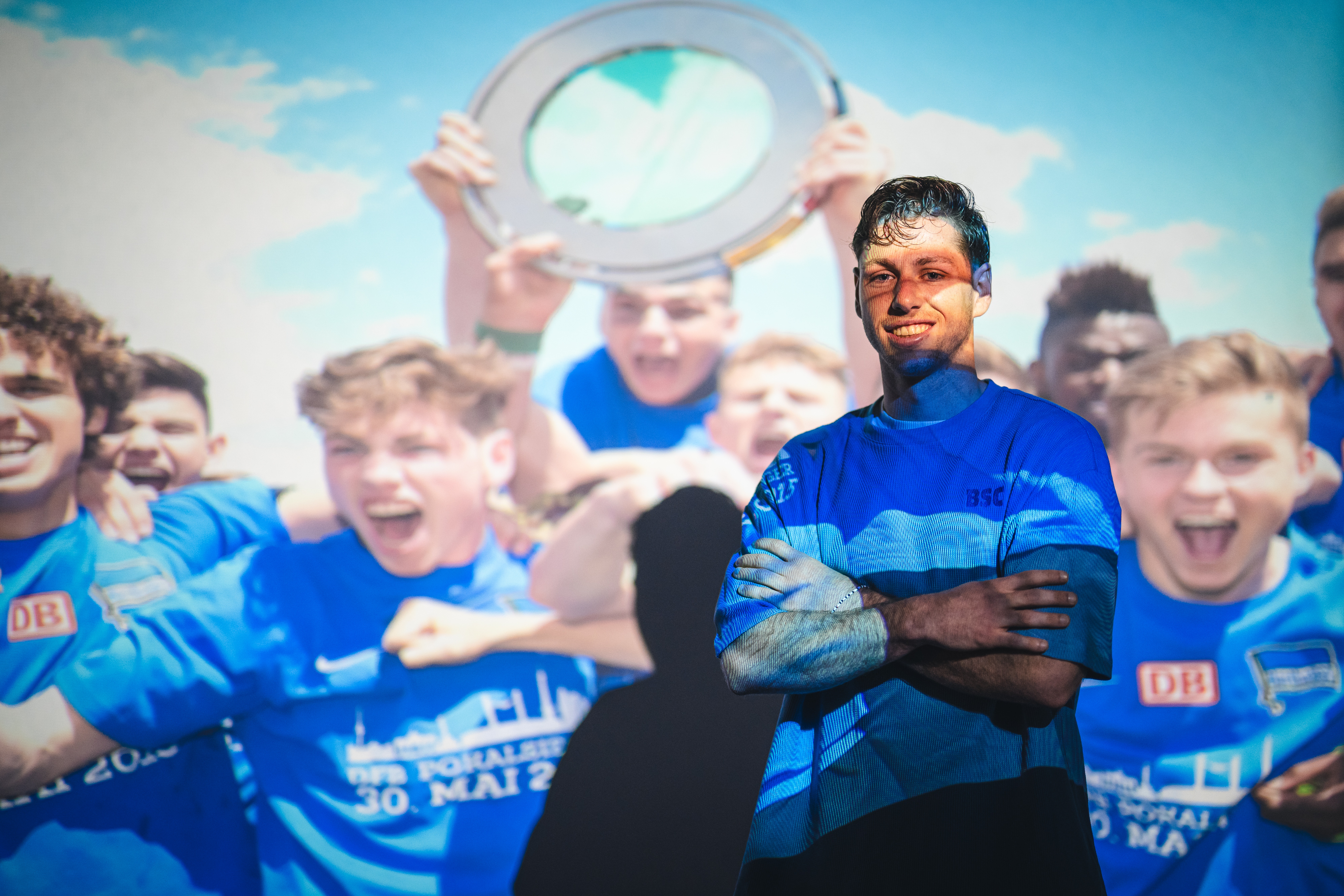 Leon Jensen steht vor einem Bild vom Pokalgewinn mit der U19.