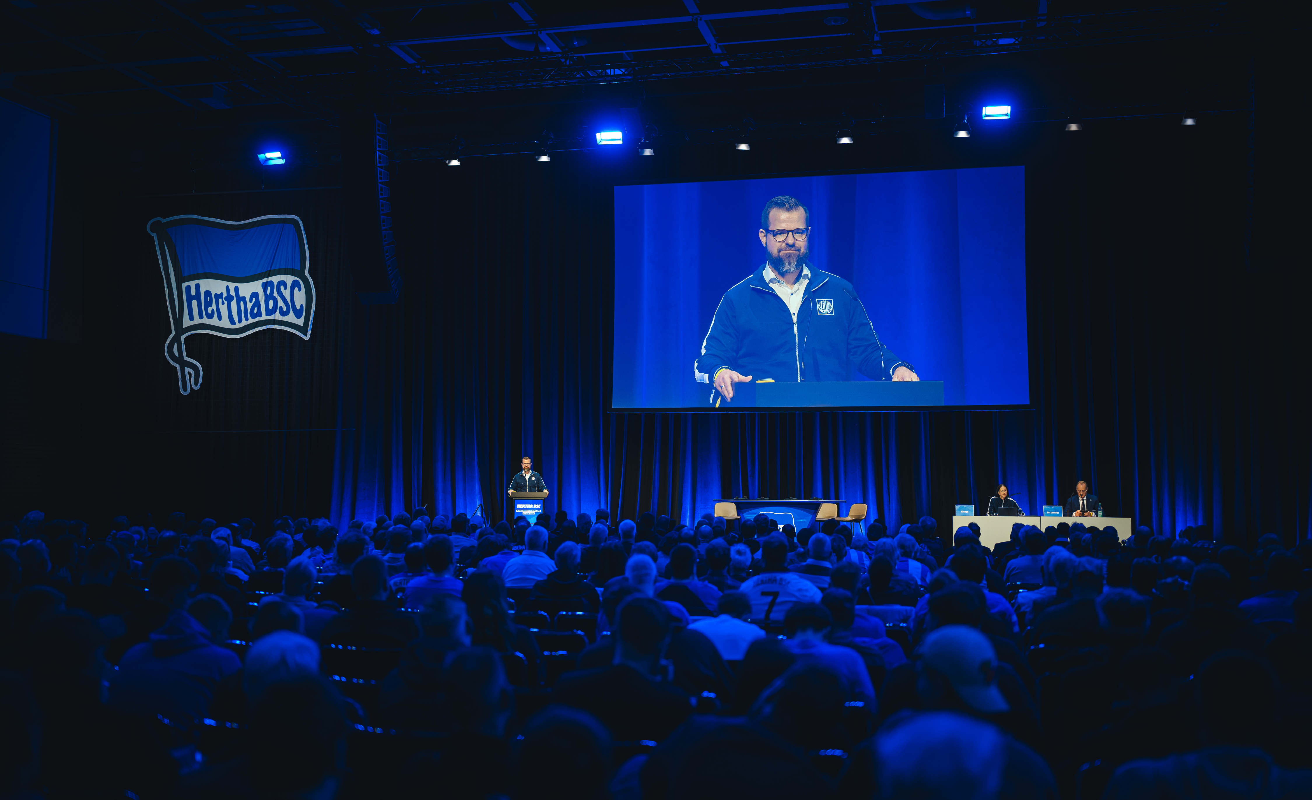 Fabian Drescher steht auf dem Podium der Messehalle und spricht zu den Mitgliedern.