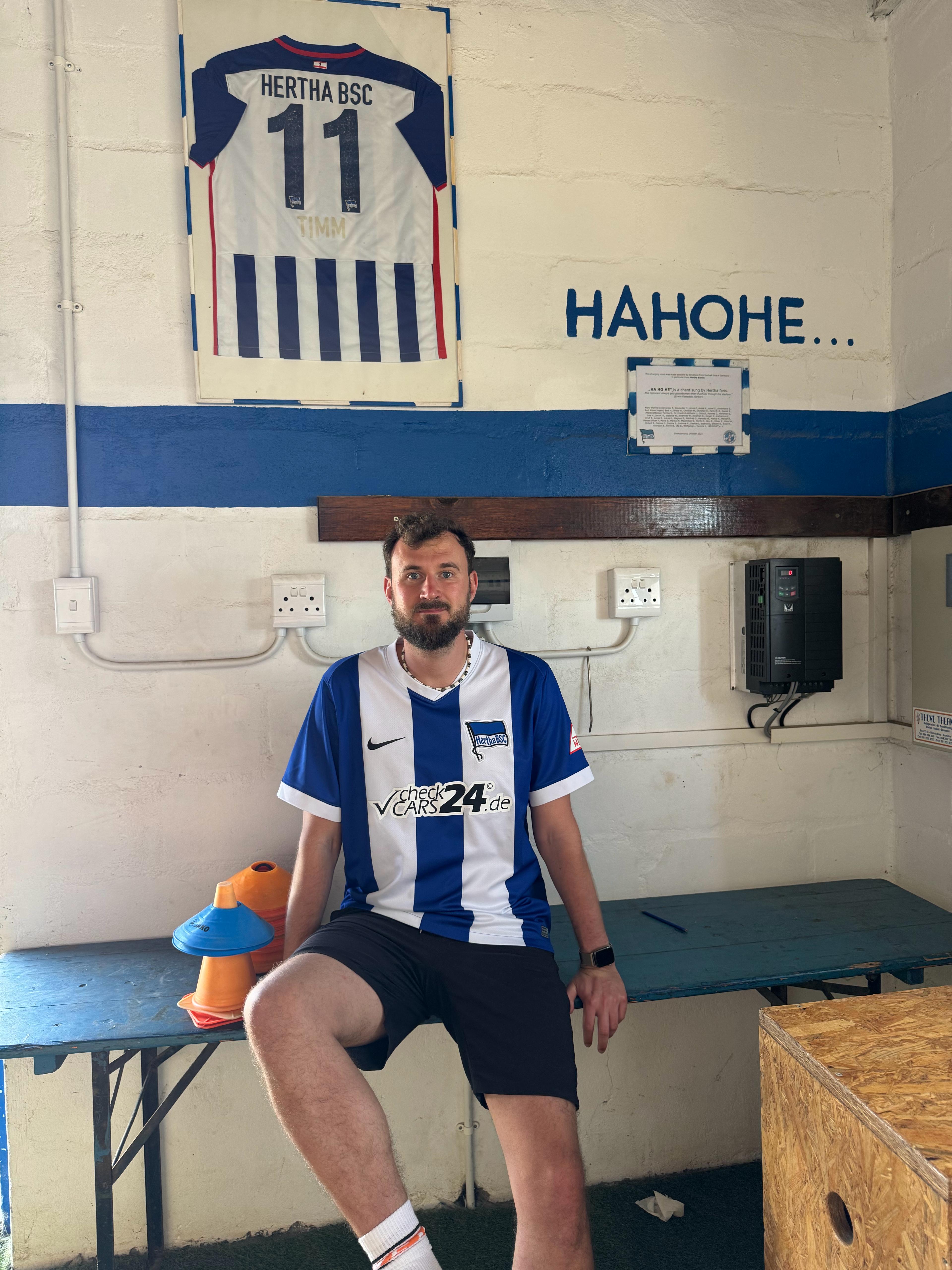 Timm Buchholz sitzt mit Hertha-Trikot in der blau-weißen Umkleidekabine.