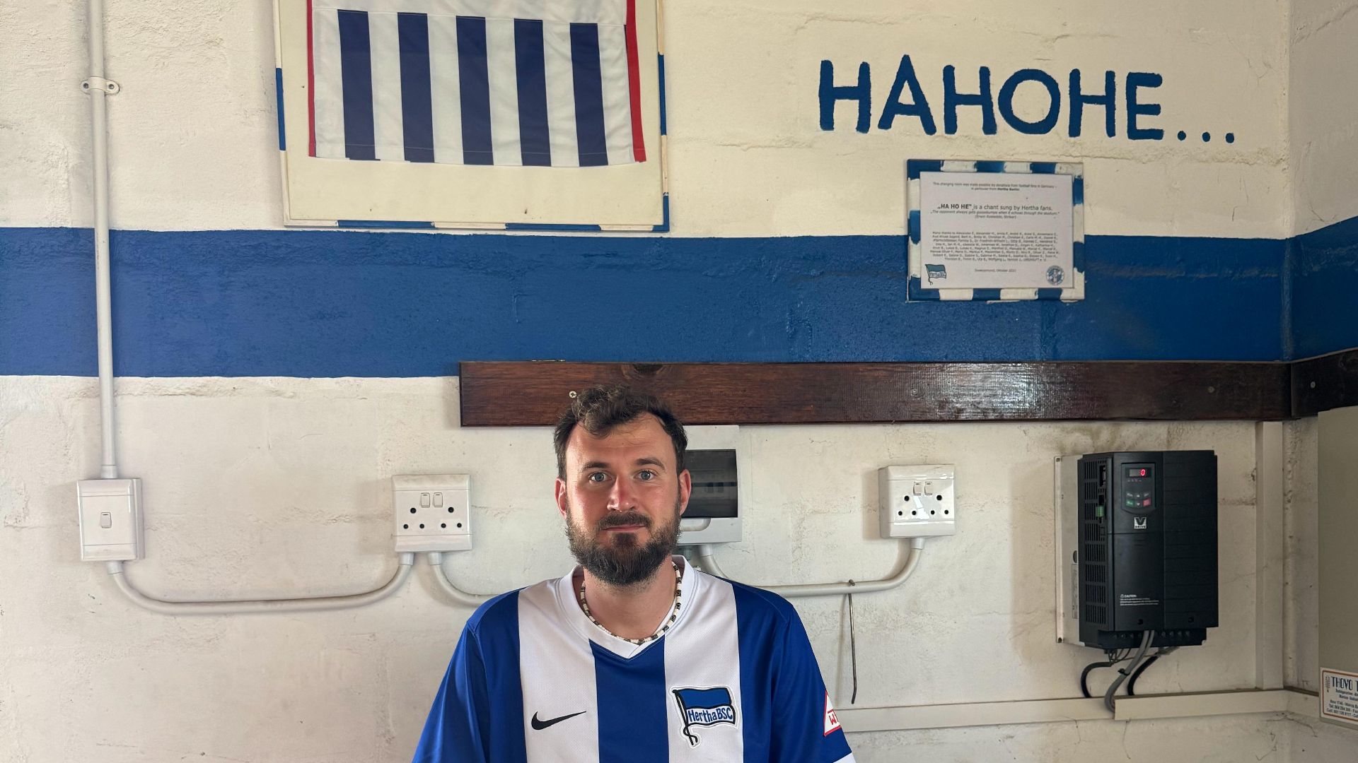Timm Buchholz sitzt mit Hertha-Trikot in der blau-weißen Umkleidekabine.