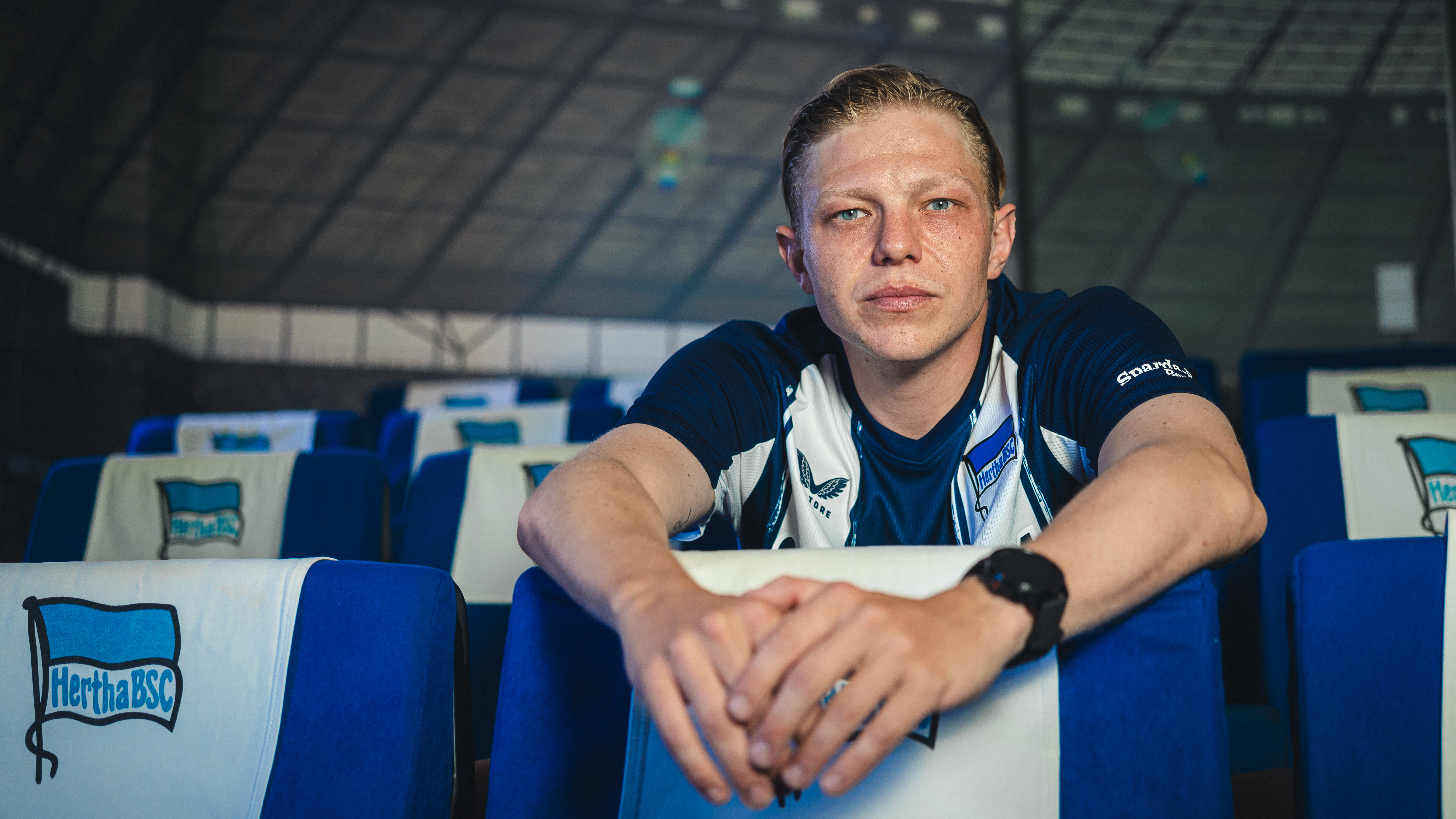 Leo Kunz sitzt zwischen blau-weiß gepolsterten Sitzen mit dem Hertha-Logo.