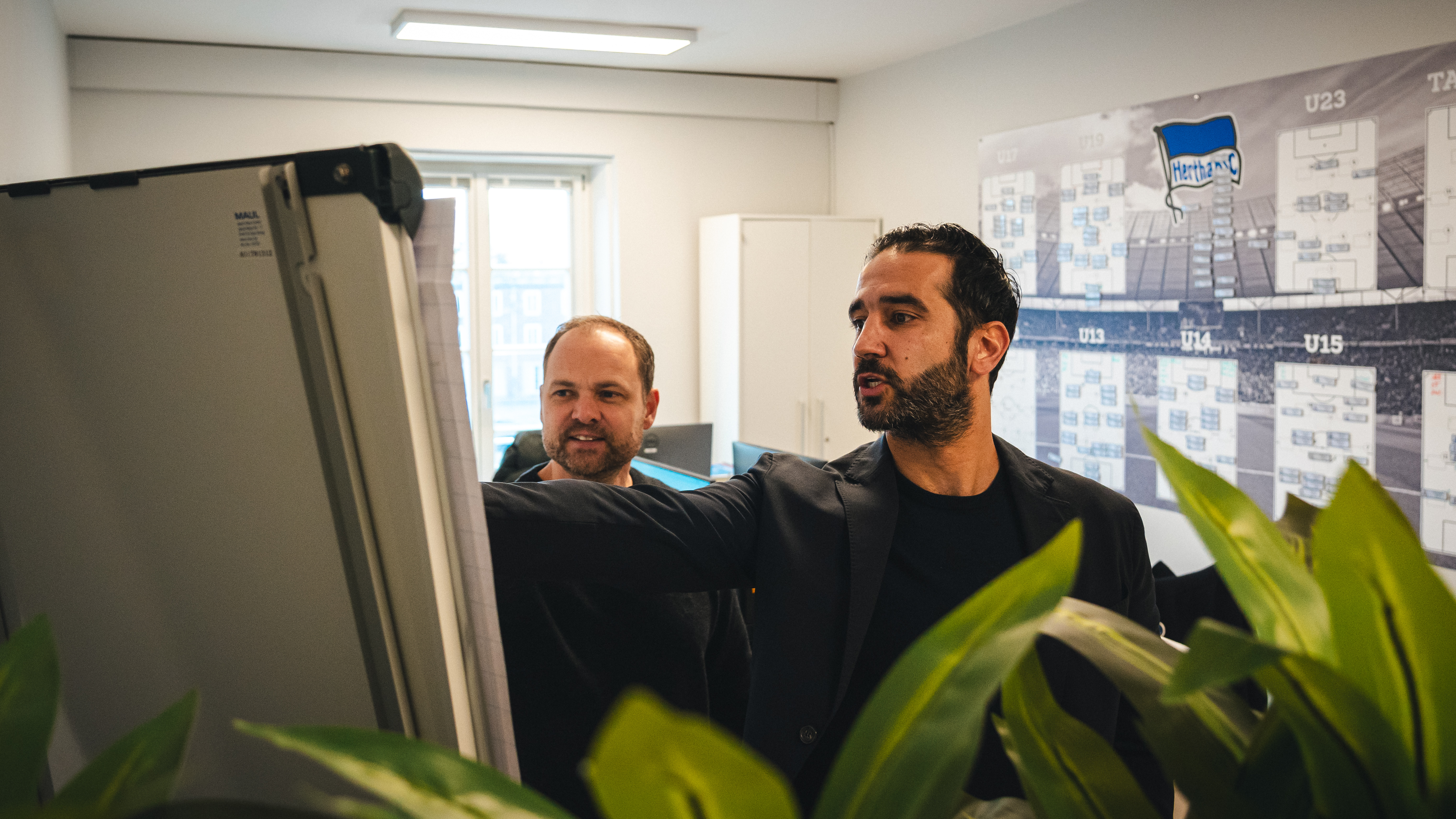 Björn Müller und Sasan Gouhari schauen in ihrem Büro auf eine Tafel.