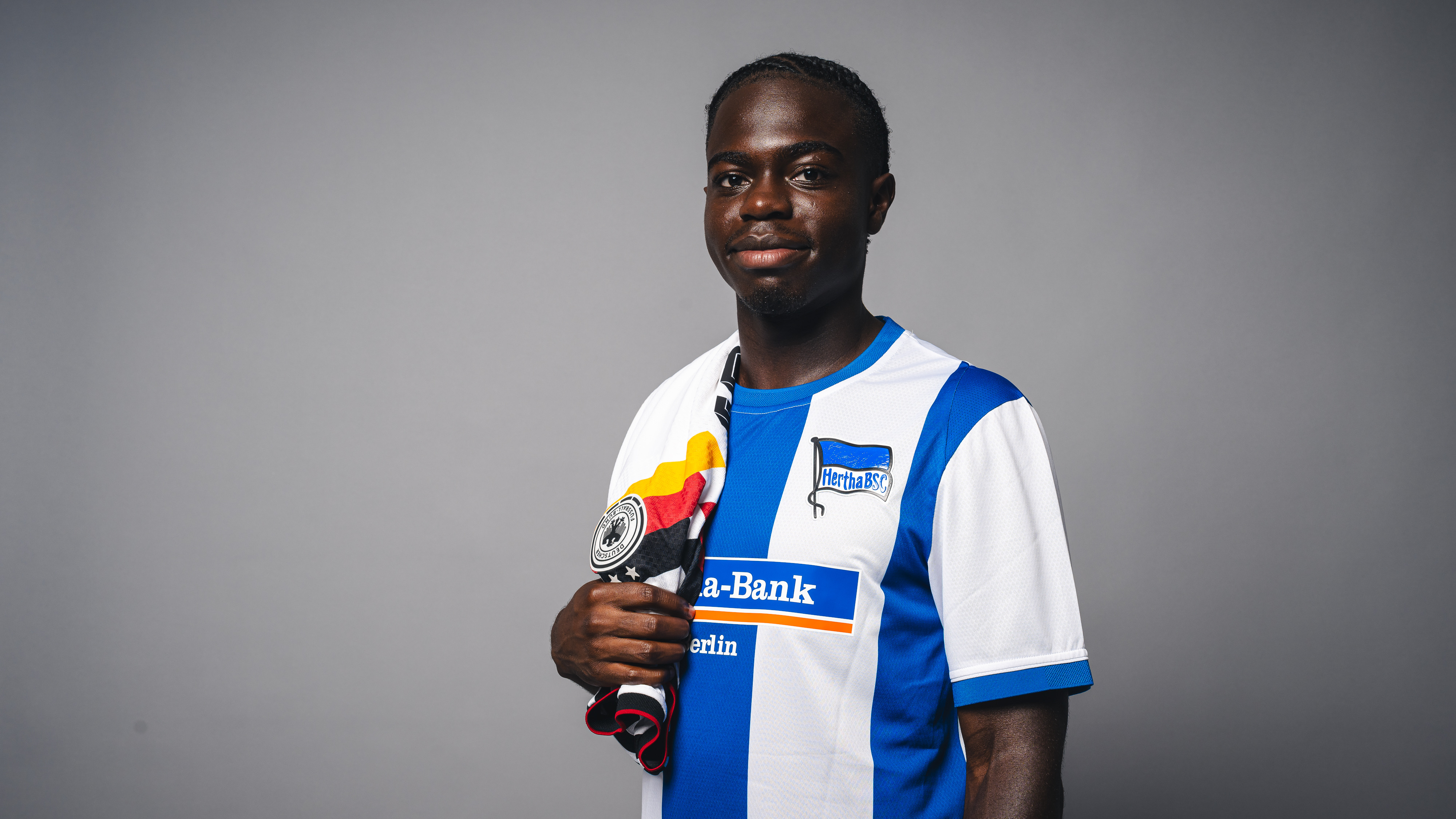 Boris Mamuzah Lum in einem Hertha-Trikot mit DFB-Trikot über der Schulter.