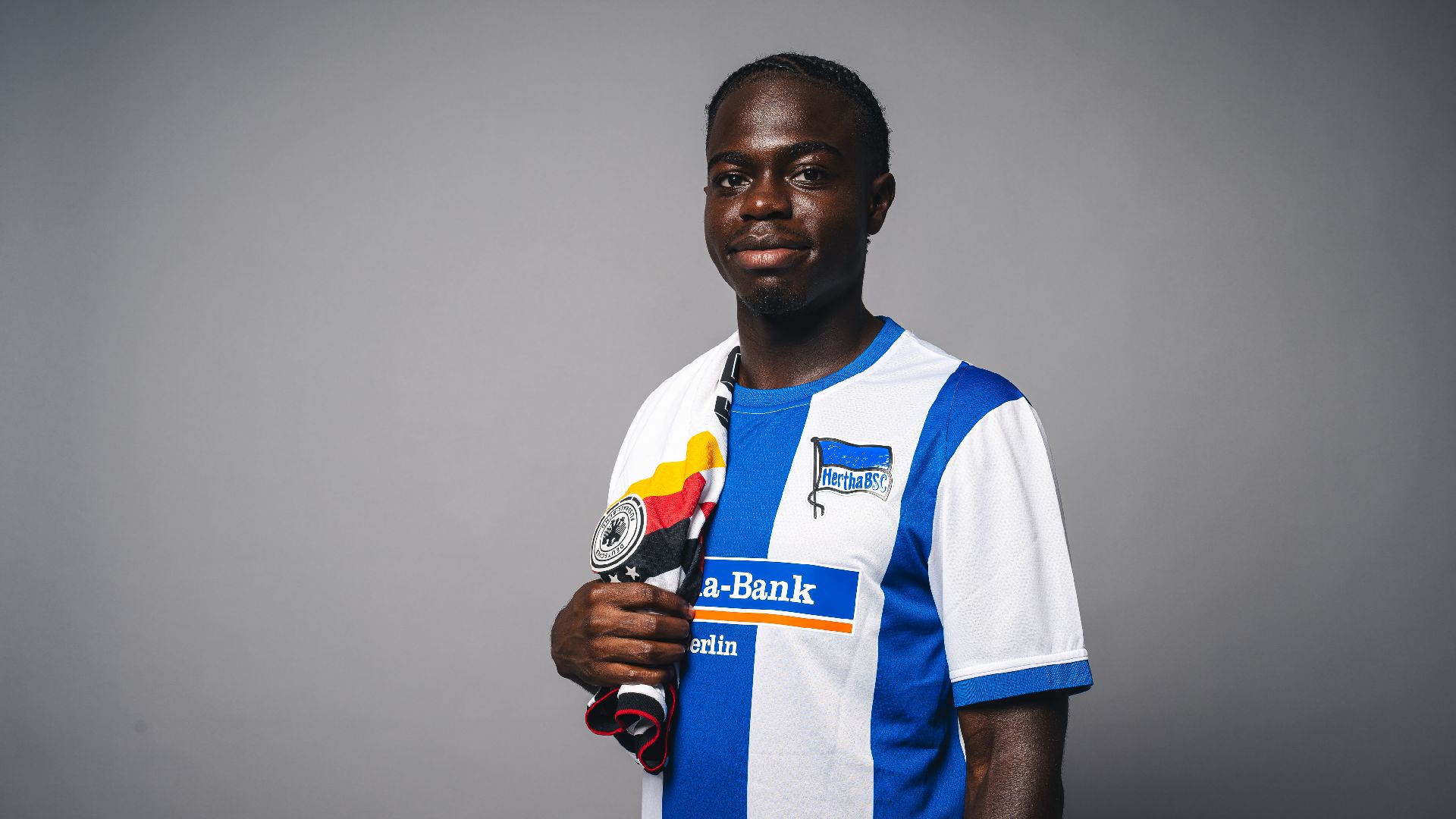 Boris Mamuzah Lum in einem Hertha-Trikot mit DFB-Trikot über der Schulter.