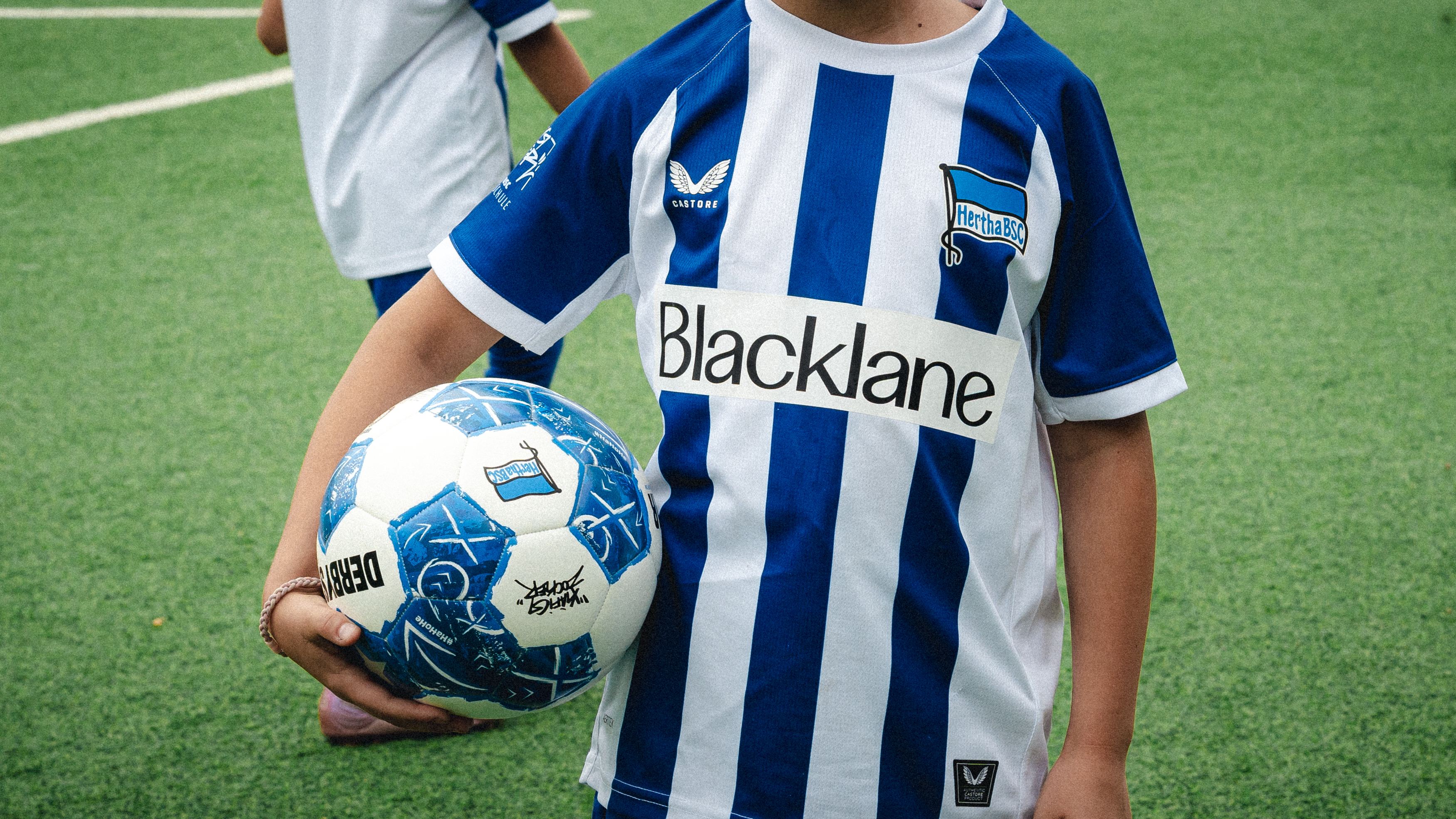 Ein Kind im blau-weißen Trikot hält einen Ball unter dem Arm.
