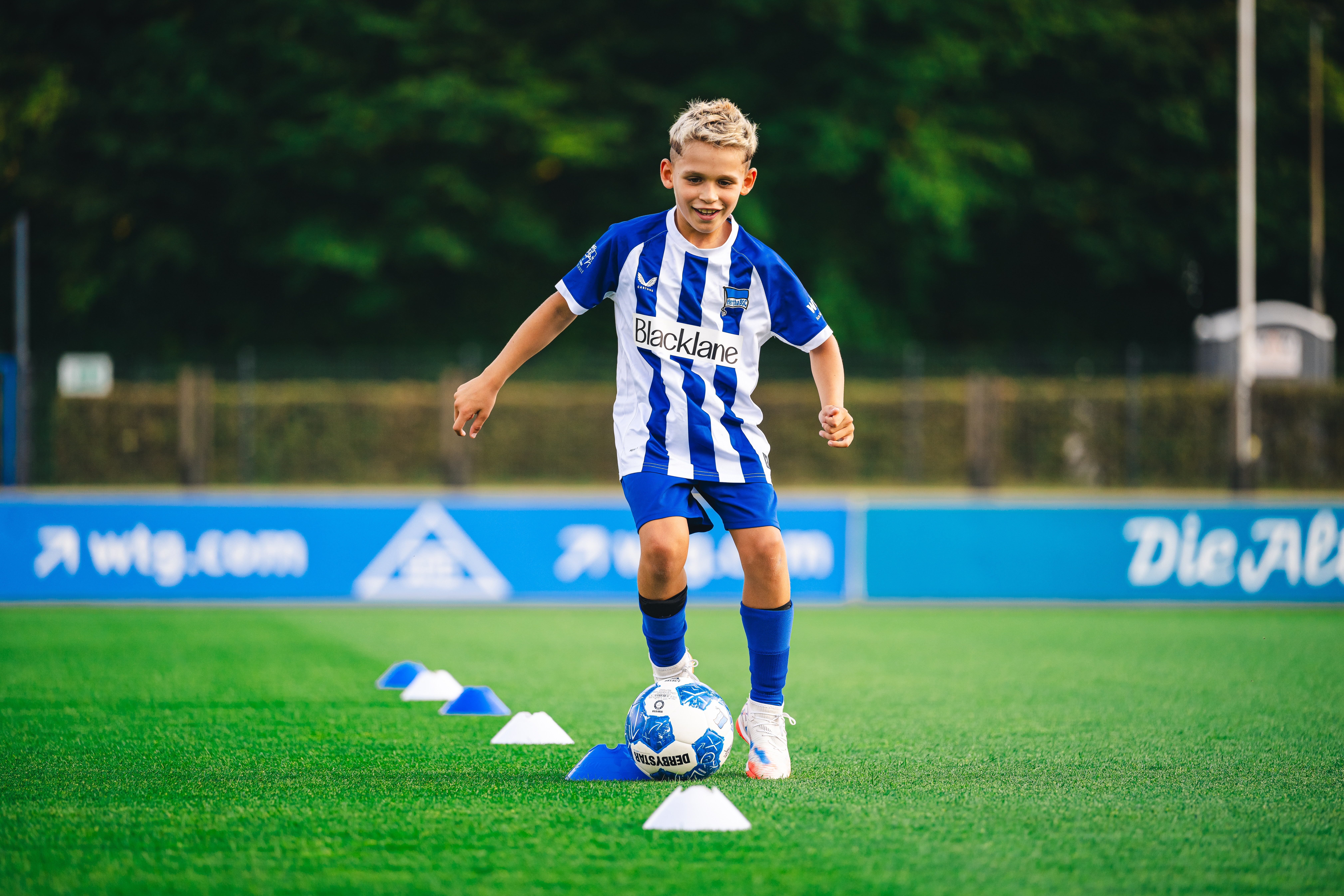 Ein Kind dribbelt mit Ball um Hütchen.