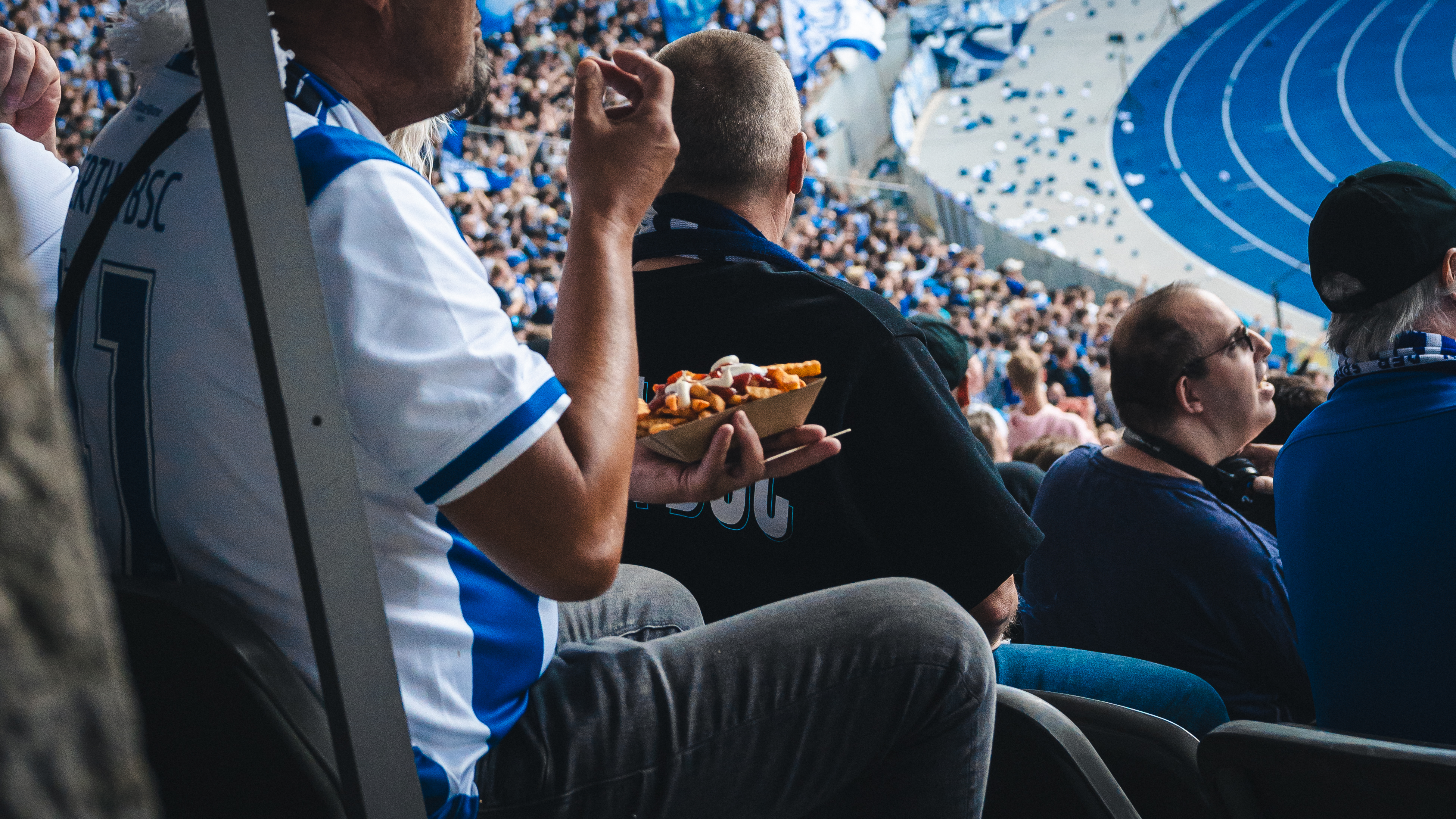 Ein Fan sitzt auf seinem Platz im Stadion und isst Pommes.