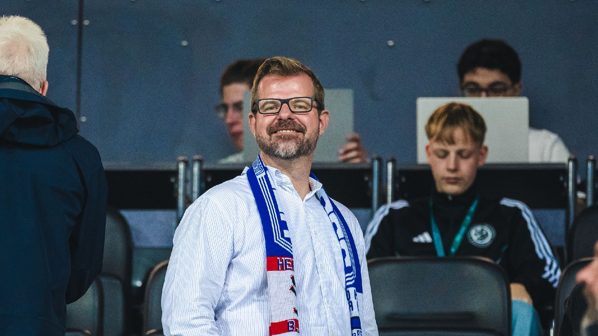Fabian Drescher lächelnd auf der Tribüne mit Hertha Schal.